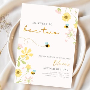 May include: A party invitation with the text "SO SWEET TO bee two" in gold script. The invitation features yellow flowers, bees, and the text "Olivia's SECOND BEE-DAY!" in a decorative font. The invitation is on a white background.
