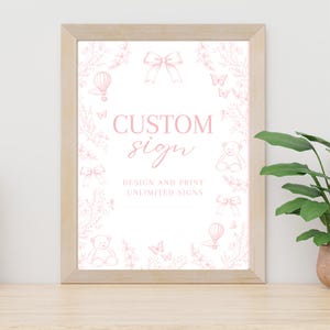 Pode incluir: Um letreiro personalizado emoldurado com acabamento em madeira clara. O letreiro apresenta ilustrações cor-de-rosa de laços, borboletas, ursinhos de pelúcia e balões de ar quente. As palavras "CUSTOM sign" estão em script rosa, com "DESIGN AND PRINT UNLIMITED SIGNS" abaixo.