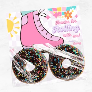 以下が含まれることがあります： ピンクのローラースケートと、カラフルなスプリンクルがかけられたチョコレートドーナツが2つ。カードには「一緒にローラースケートに乗ってくれてありがとう！」と書いてあり、太陽と虹のデザインが描かれている。