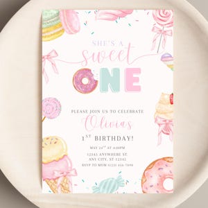 Puede incluir: Una invitación de cumpleaños en tonos pastel con el texto "She's a Sweet One". El diseño incluye ilustraciones de dulces como rosquillas, piruletas, conos de helado y macarons. La invitación es para el primer cumpleaños de Olivia.