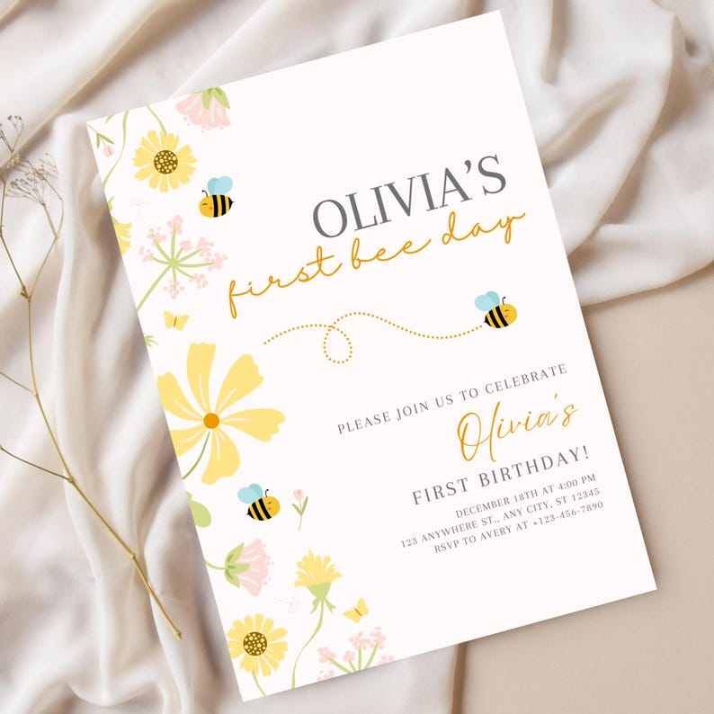 May include: A white invitation card with the text "OLIVIA'S first bee day" in gold and gray. The card is decorated with yellow flowers, pink accents, and cartoon bees. The invitation is for Olivia's first birthday.