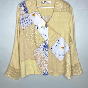 May include: A yellow, long-sleeved, patchwork blouse with a V-neck and a button closure. The blouse is made of a lightweight fabric and features a variety of floral prints and textures.