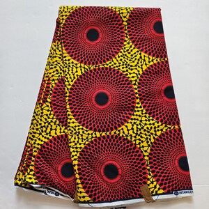 May include: Red, yellow and black African wax print fabric with a circular pattern. The fabric is folded in half and has a white border.