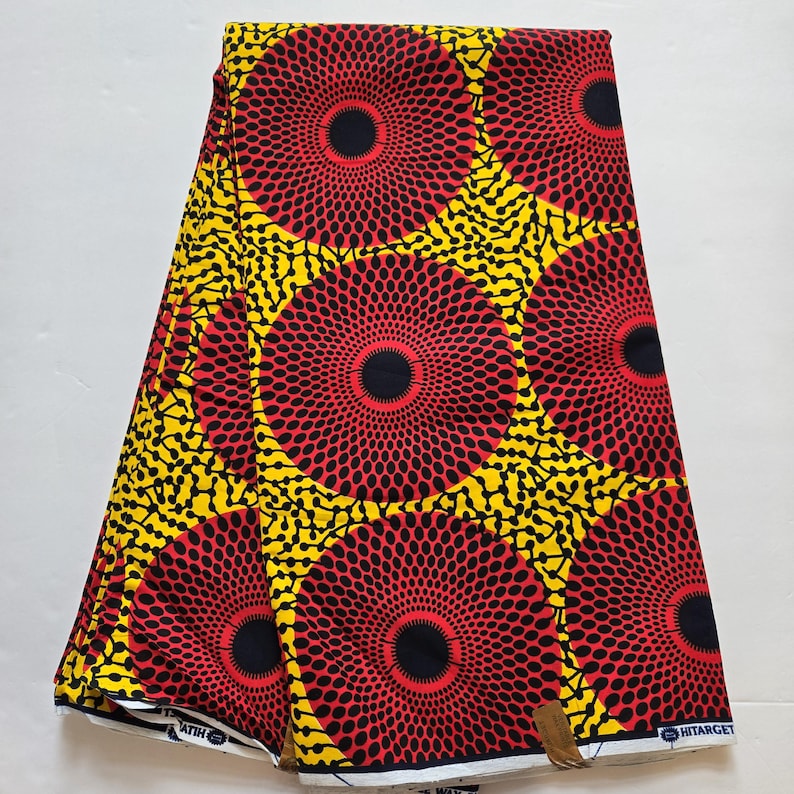 May include: Red, yellow and black African wax print fabric with a circular pattern. The fabric is folded in half and has a white border.