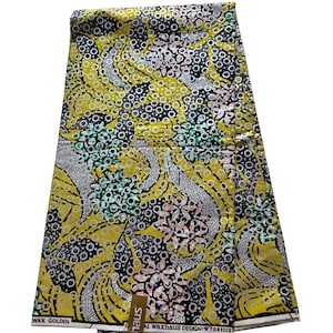May include: A folded fabric with a vibrant yellow background, featuring a repeating pattern of black, white, pink, and green floral and circular designs. The fabric has the text "WAX GOLDEN" and "AL waxhaus DESIGN: W7081113".