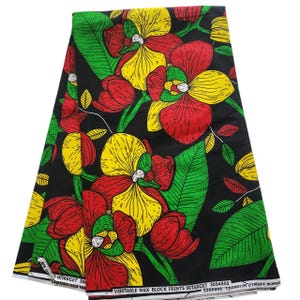 Op de afbeelding: Zwarte stof met een opvallend bloemmotief van rode, gele en groene bloemen en bladeren. De stof is bedrukt met de tekst "VERITABLE WAX BLOCK PRINTS HITARGET 3004802 GUARANTEED WA".