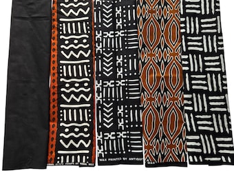 May include: A collection of colorful African wax print fabrics. The fabrics feature geometric and abstract patterns in black, white, orange, and brown. The text "WAX PRINTED BY ANTIQUE" is visible on one of the fabrics.