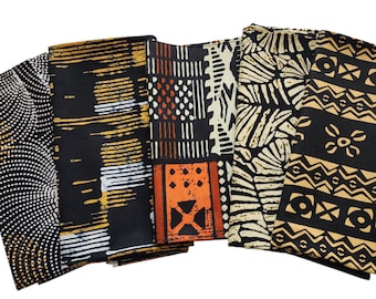 May include: A collection of folded fabric pieces with various African-inspired patterns. The fabrics feature designs in black, white, orange, and gold. Patterns include dots, stripes, and geometric shapes, creating a diverse and colorful display.