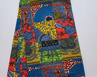 May include: A vibrant fabric with a patchwork design featuring blue, red, yellow, and green geometric patterns. The fabric includes text that reads "BLOCK PRINTS HITARGET GUARANTEED" and "VERITABLE WAX BLOCK PINTS HITARGET 1753415".