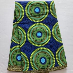 May include: A blue and green fabric with a repeating pattern of concentric circles. The circles are made up of yellow, green, red, and blue dots. The fabric has a woven texture and is folded in half.