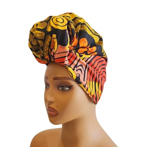 May include: A colorful head wrap featuring a vibrant pattern of orange, yellow, and black abstract shapes. The fabric is wrapped and tied to create a turban-style head covering. The head wrap is designed to be worn on the head.