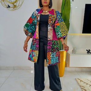 May include: A long-sleeved, open-front jacket featuring a vibrant, multi-colored patchwork pattern with geometric and animal print motifs, worn over a solid black sleeveless jumpsuit with wide-leg trousers and a simple round neckline.