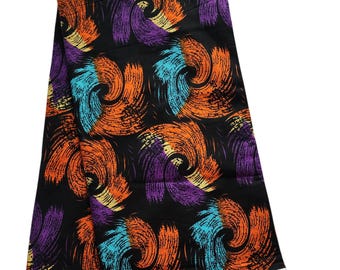 May include: A folded black fabric with a repeating pattern of swirling brushstrokes in orange, purple, and turquoise. The fabric has a white border and a brown tag. The pattern is reminiscent of abstract art.