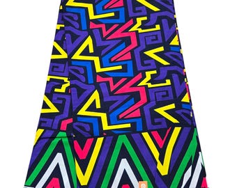 Op de afbeelding: Een kleurrijke stof met een geometrisch patroon in tinten geel, blauw, roze, groen en wit op een zwarte achtergrond. De stof heeft een herhalend patroon van abstracte vormen en lijnen.