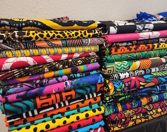 May include: A stack of colorful fabric bolts with various patterns. The fabrics display a range of colors, including yellow, red, pink, green, and blue, with designs such as polka dots, floral, and geometric shapes. The bolts are neatly arranged, showcasing the variety of textiles.