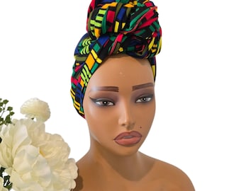 May include: A colorful head wrap with a geometric pattern in shades of red, yellow, green, and blue. The wrap is tied in a bun on top of the head.