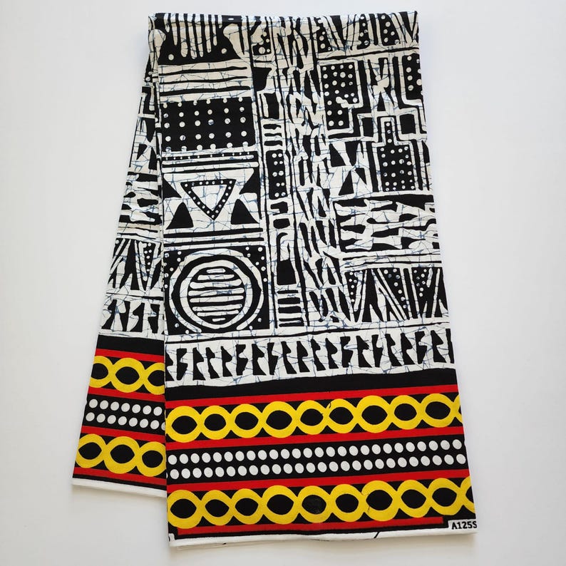 May include: Folded fabric with a bold black and white geometric pattern. The design includes circles, triangles, and rectangular shapes. The bottom edge features a border of yellow and red circles and dots.