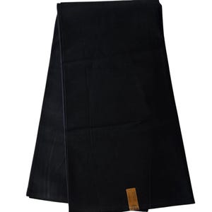 May include: A black fabric table runner with a brown tag attached to the bottom right corner.