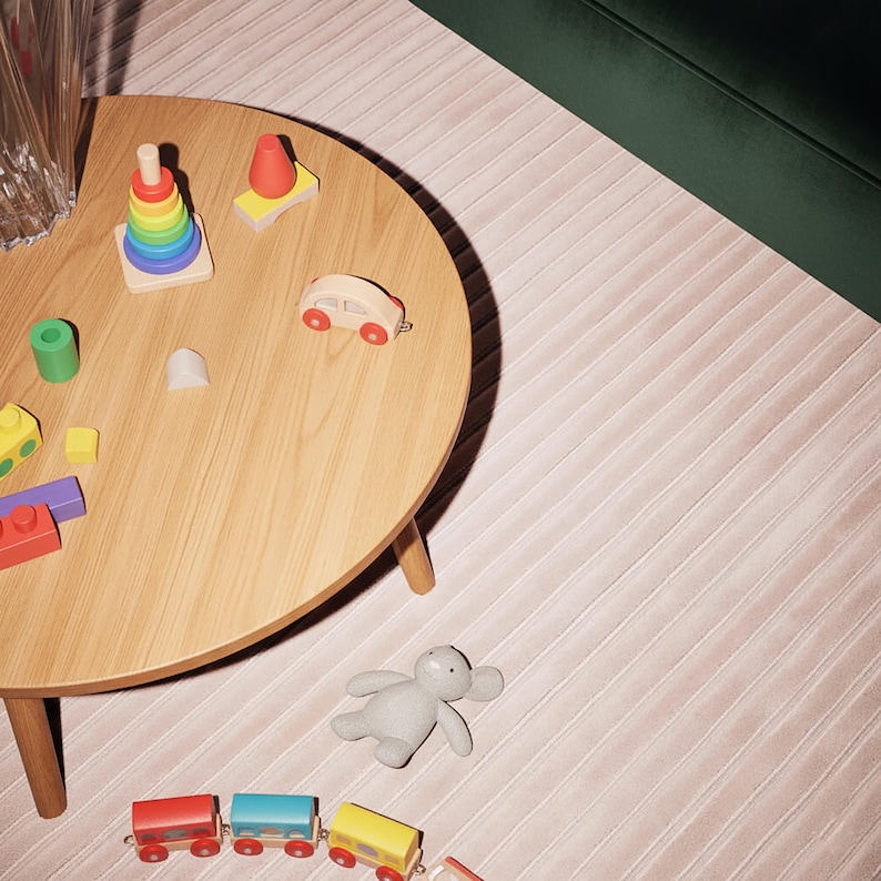 May include: A wooden round table displays colorful wooden toys, including a rainbow stacking ring, a red and white car, and a toy train. A gray stuffed animal and a pink striped rug are also visible.