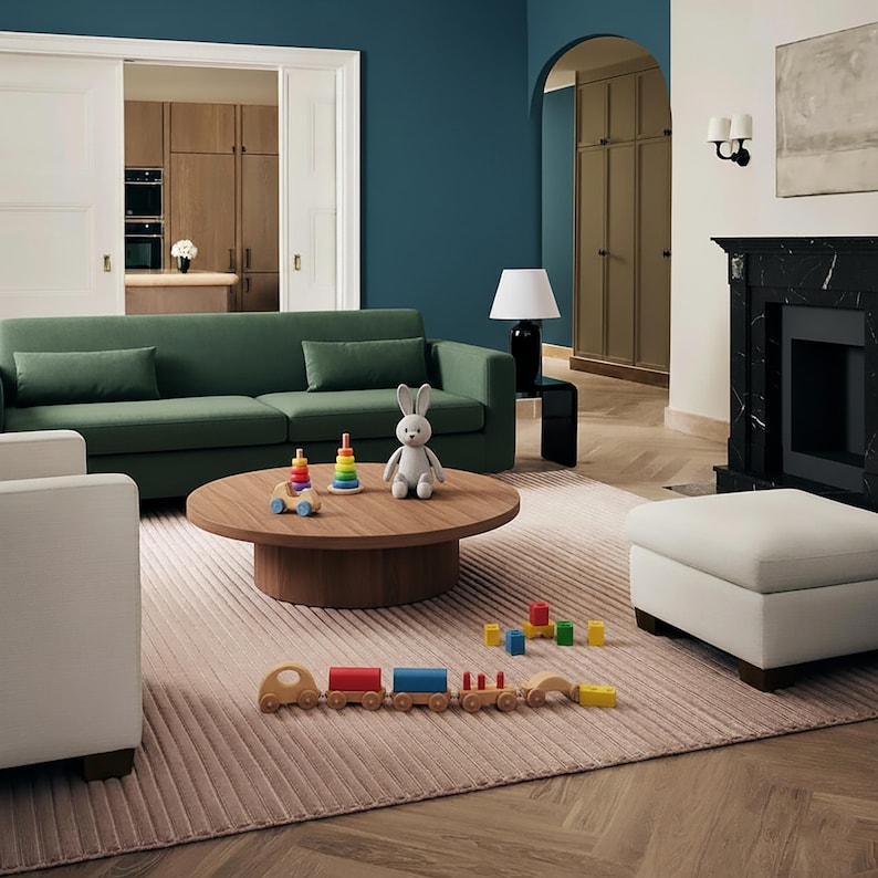May include: A living room scene with a green sofa, a round wooden coffee table, and a light pink rug. Toys, including a wooden train and a stuffed bunny, are on the rug and table. The room has a modern design with a fireplace and a white ottoman.