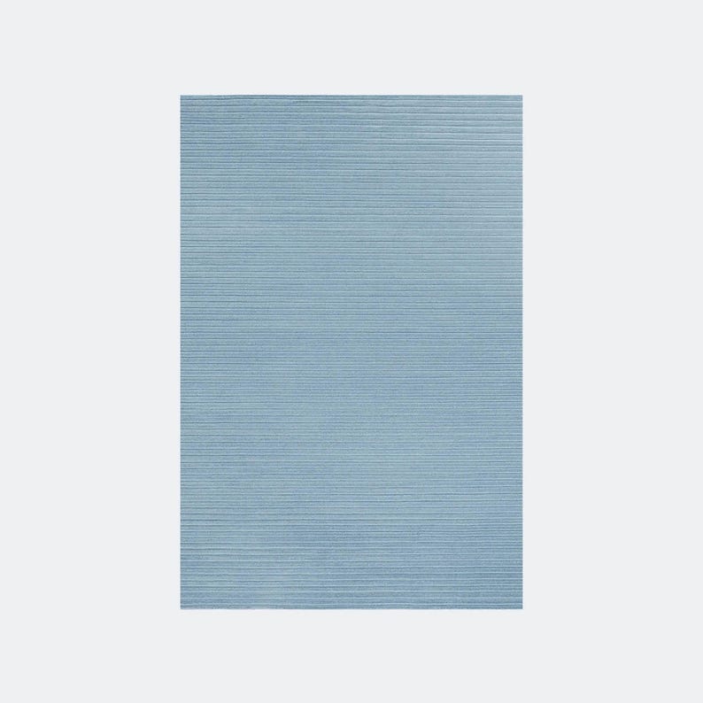 May include: A rectangular, light blue rug with a textured, ribbed surface. The rug's design features horizontal lines, creating a subtle pattern. The color is a soft, muted blue, suitable for various interior design styles.