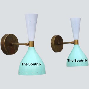 Puede incluir: Dos apliques de pared con una pantalla cónica blanca y una pantalla en forma de campana perforada de color verde azulado. Las lámparas tienen una base y un brazo de latón. El texto "The Sputnik" está impreso en las pantallas.