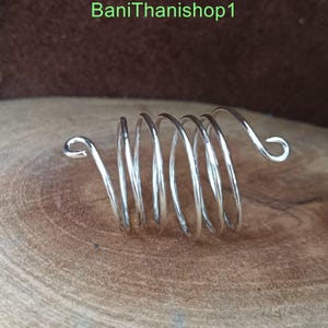 Puede incluir: Un anillo de espiral plateado con un extremo curvo. El anillo est&aacute; hecho de m&uacute;ltiples espirales de alambre.