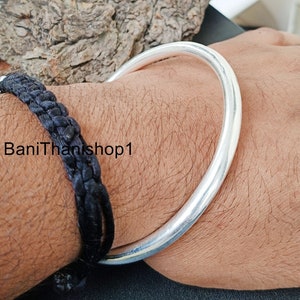 May include: A silver bangle bracelet on a person's wrist. The bracelet is thick and round, and it has a smooth, polished finish.