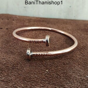 May include: A copper bracelet with a nail design. The bracelet is open and has a simple, minimalist style.