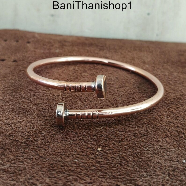 May include: A copper bracelet with a nail design. The bracelet is open and has a simple, minimalist style.