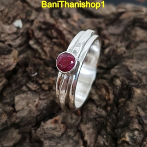 May include: A silver ring with three bands and a red gemstone in the center.