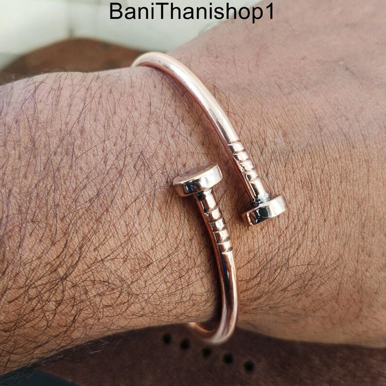 May include: A rose gold bangle bracelet with a nail design. The bracelet is open and has a simple, elegant design.