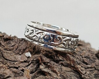 May include: A silver spinning ring with a floral design. The ring is made of two bands that spin independently.