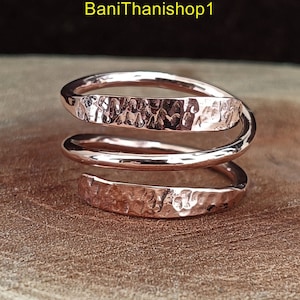 May include: A rose gold hammered copper ring with a triple spiral design. The ring is made of three bands of copper that are twisted together to create a unique and stylish look.