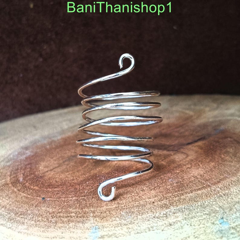 Puede incluir: Anillo de espiral de plata con un dise&ntilde;o &uacute;nico. El anillo est&aacute; hecho de m&uacute;ltiples bobinas de alambre que se retuercen juntas para crear una forma de espiral. El anillo tiene un dise&ntilde;o simple y elegante que lo convertir&iacute;a en un gran regalo para cualquier ocasi&oacute;n.