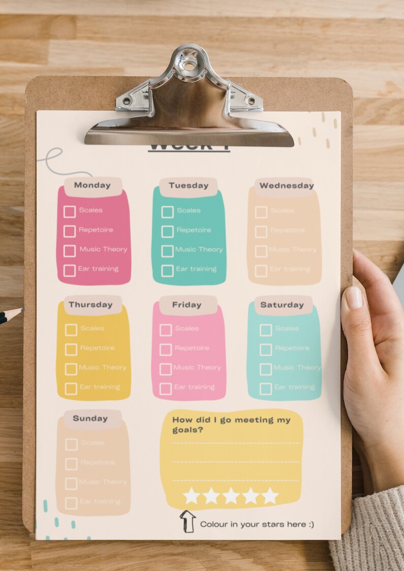 May include: A weekly music practice planner on a clipboard with a metal clip. The sheet features colourful daily sections for Monday through Sunday, each with checkboxes for Scales, Repertoire, Music Theory, and Ear training, plus a goal review section.