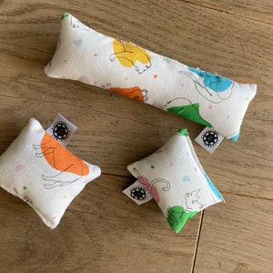 May include: Three white fabric catnip toys with colorful animal illustrations and black and white labels. The toys are shaped like a long rectangle and two squares.