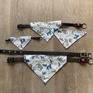 May include: Three different sizes of dog bandanas with a white background and a pattern of various animals in brown, tan, and black. The bandanas are attached to black and brown collars with a red clip.