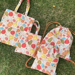 May include: Three reusable shopping bags with a cream background and a colorful pumpkin and squash pattern. The bags are made of fabric and have different styles, including a tote bag, a drawstring bag, and a smaller tote bag.