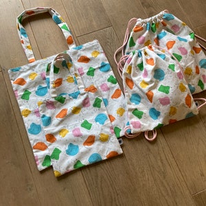 May include: Five reusable shopping bags with a white background and a colorful print of cartoon cats. The bags are made of cotton and have a drawstring closure.