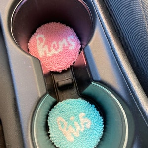 May include: Two round, fuzzy car coasters with the words "Mom" and "Dad" embroidered in white on a pink and blue background.