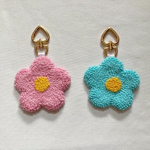 May include: Two flower-shaped keychains with gold heart-shaped clasps. One keychain is pink with a yellow center, and the other is blue with a yellow center.