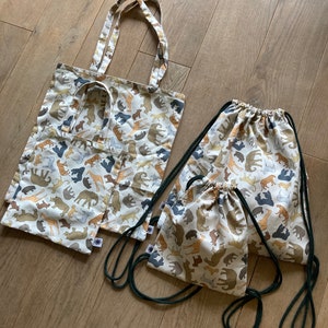 Puede incluir: Tres bolsas de la compra reutilizables con fondo blanco y un patrón de varios animales en marrón, negro y beige. Las bolsas están hechas de un tejido de algodón suave.