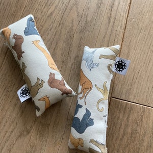 Puede incluir: Dos almohadas rectangulares de tela con fondo blanco y un patrón de varios animales en marrón, beige y gris. Las almohadas tienen una pequeña etiqueta circular con un diseño de flor y el texto "PATTERN CULTURE".