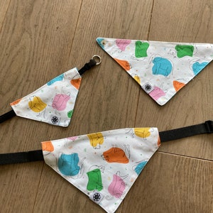 May include: Three white fabric dog bandanas with a colorful print of cartoon animals. The bandanas are triangular and have black adjustable straps.
