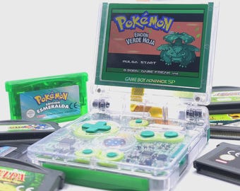 May include: A clear Game Boy Advance SP console with green accents and a screen displaying "Pokémon Edición Verde Hoja." Several game cartridges, including "Pokémon Esmeralda," are visible. The console's buttons and D-pad are green.