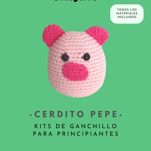 May include: Pink crocheted pig amigurumi toy with black eyes and a pink nose. The toy is part of a beginner crochet kit. The text "TODOS LOS MATERIALES INCLUIDOS" and "•CERDITO PEPE. KITS DE GANCHILLO PARA PRINCIPIANTES" is visible on the image. The text "WWW.THESNUGLIES.COM" is also visible on the image.