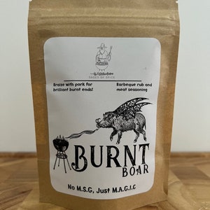 May include: A brown paper bag with a white label. The label features a black and white illustration of a boar with wings. The text on the label reads "SAGES OF SPICE", "Braize with pork for brilliant burnt ends!", "Barbeque rub and meat seasoning", "BURNT BOAR", and "No M.S.G. Just M.A.G.I.C."