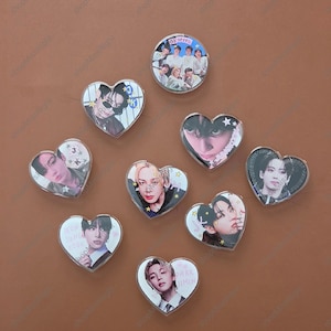 May include: A collection of nine acrylic pins featuring portraits of K-pop artists. Eight pins are heart-shaped and one is circular. The circular pin displays a group photo with the text "my seven". Individual pins feature portraits with text like "JK", "JUNGKOOK", and "PARK JIMIN".