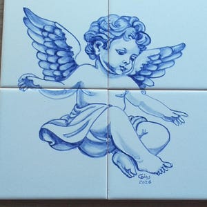 Peut inclure: Un ensemble de quatre carreaux de céramique blancs carrés disposés en grille, présentant une illustration peinte à la main en bleu d'un chérubin ailé. Le chérubin est représenté assis, et le carreau en bas à droite porte la signature Gias 2026.